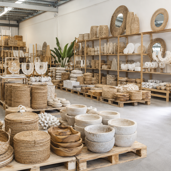 Wicker and stone bowls on pallets in a warehouse setting with shelves in the background.